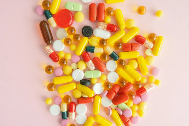 a pile of assorted pills on a pink surface, by Olivia Peguero, pexels, red and yellow scheme, complexly detailed, syringes, candy treatments