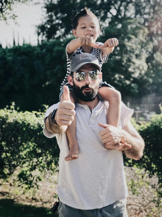 a man holding a child on his shoulders, pexels contest winner, wearing sunglasses and a cap, thumb up, thick black beard, 🚿🗝📝