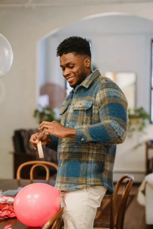 a man standing in front of a table with balloons, happening, flannel, jaylen brown, holding gift, subtle detailing