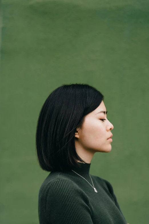 a woman standing in front of a green wall, an album cover, inspired by Fei Danxu, pexels contest winner, headshot profile picture, short green bobcut, human staring blankly ahead, angle profile portrait