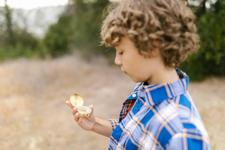 a young boy holding a piece of food in his hand, an album cover, by Kristin Nelson, pexels contest winner, pocket watch, in nature, large shell, shiny gold