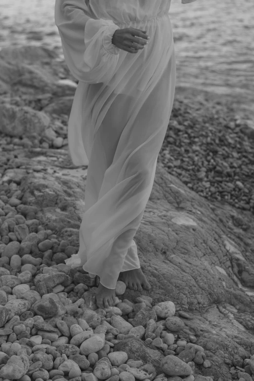 a black and white photo of a woman in a long dress, inspired by Max Dupain, unsplash, bare foot, rocks, white clothes, detail