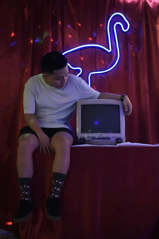 a woman sitting on top of a table next to a computer, inspired by Nan Goldin, video art, asian male, neon outlines, imgur, teenage boy