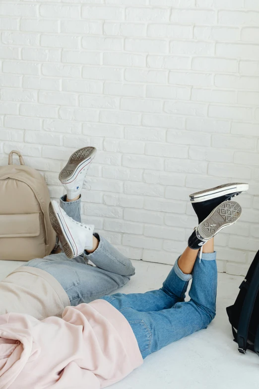 a couple of people laying on top of a bed, trending on pexels, blue jeans and grey sneakers, bags on ground, pastel style, at college