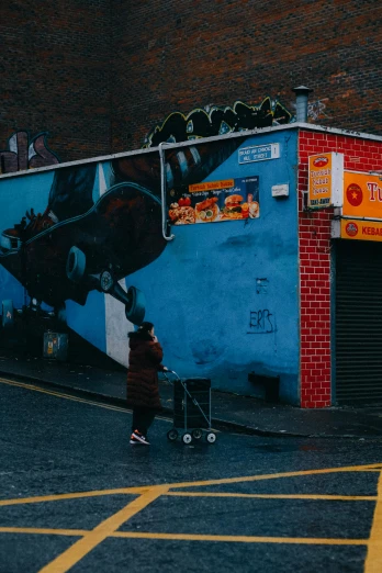 a person walking down a street next to a building, by Eamon Everall, pexels contest winner, street art, vibrant but dreary blue, shops, red wall, panoramic view of girl