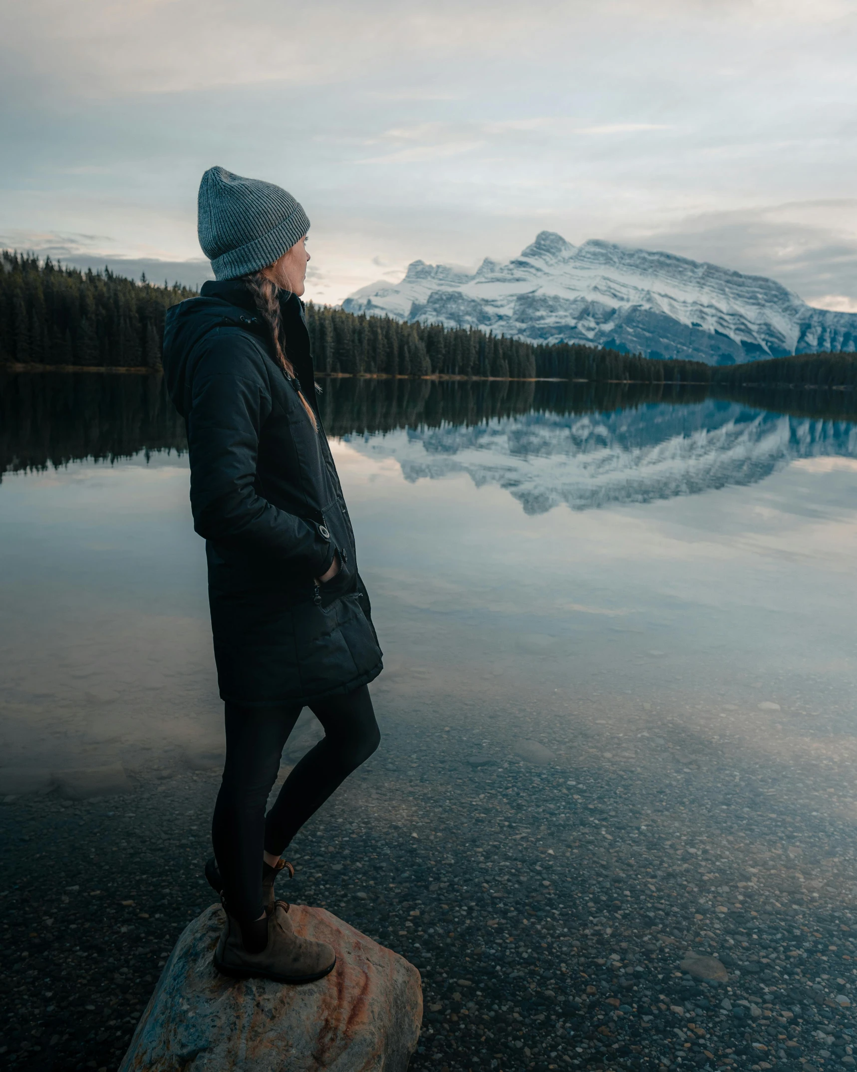 a woman standing on a rock in front of a lake, by Emma Andijewska, he also wears a grey beanie, banff national park, photo of margot robbie, cold freezing nights