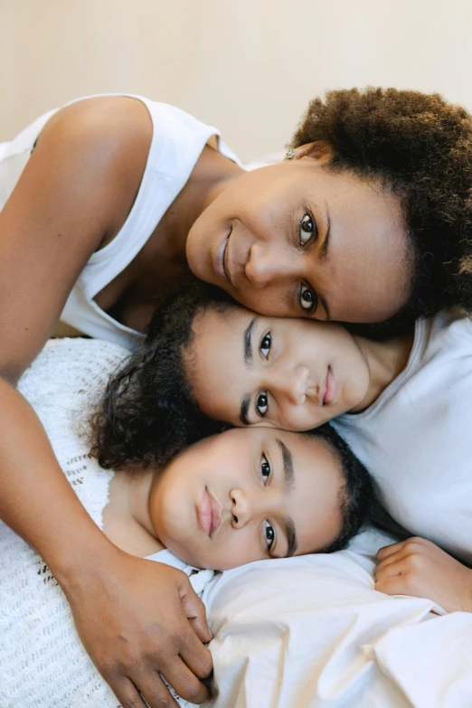 a couple of women laying on top of a bed, by Lily Delissa Joseph, pexels, portrait of family of three, brown skin, motherly, full close-up portrait