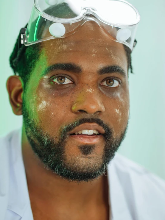 a man with a pair of goggles on his head, inspired by Ismail Gulgee, pexels contest winner, wearing a labcoat, eye color green, scruffy looking, oil slick