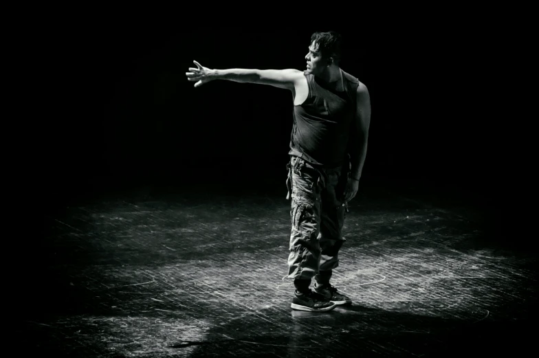 a black and white photo of a man on a skateboard, figuration libre, contemporary dance, standing in a dimly lit room, indistinct man with his hand up, till lindemann