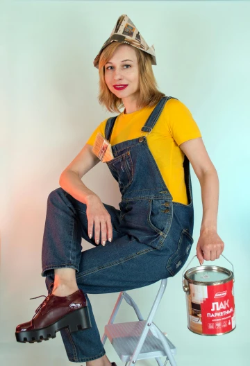 a woman sitting on a chair with a bucket of paint, inspired by Norman Rockwell, trending on pexels, wearing overalls, wearing a modern yellow tshirt, cosplay photo, mid 2 0's female