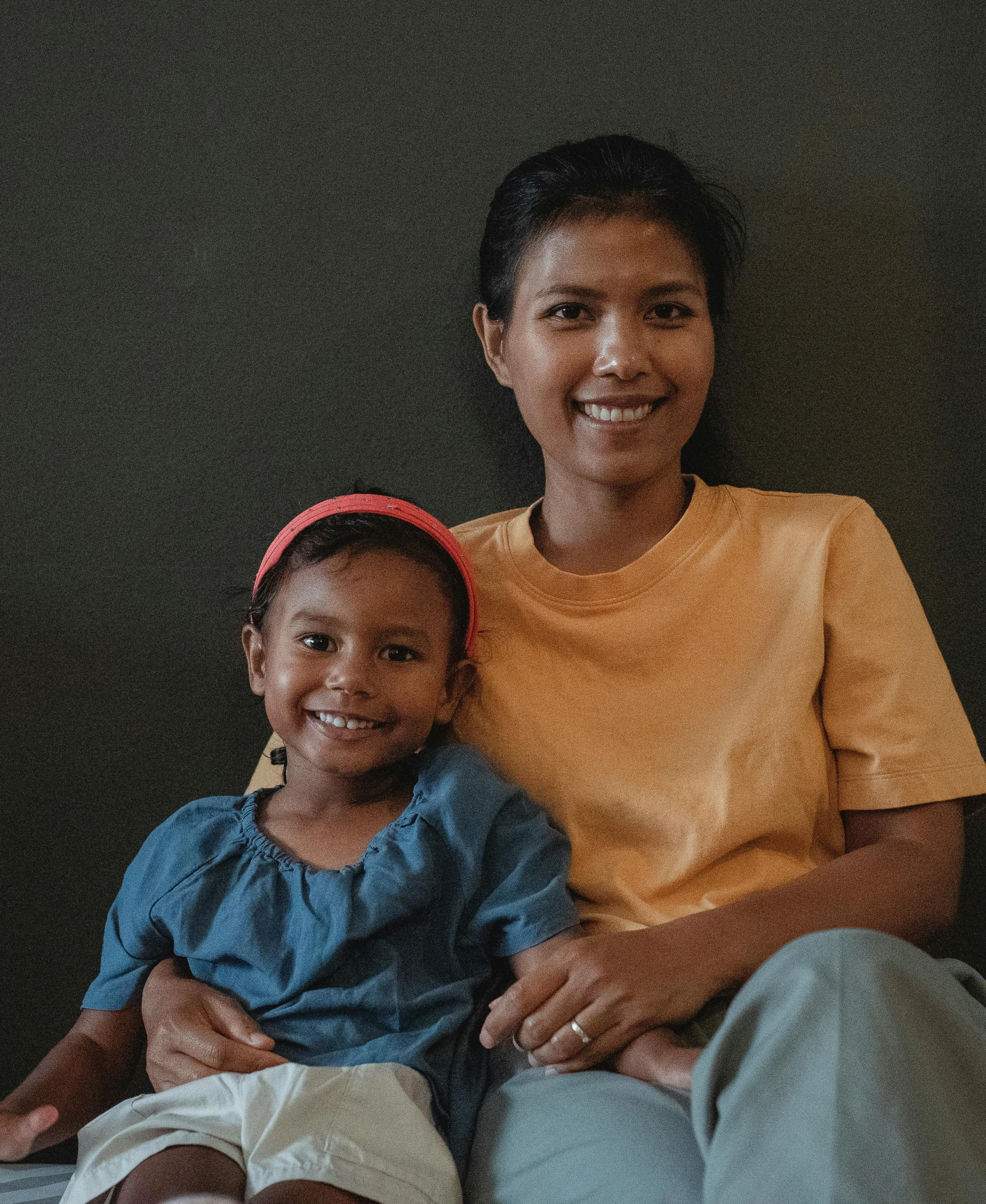 a woman sitting next to a little girl on a bed, pexels contest winner, sumatraism, plain background, proud smile, sitting in a waiting room, portrait n - 9