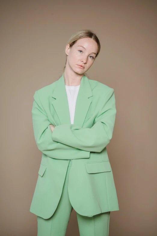 a woman in a green suit standing with her arms crossed, an album cover, by Eleanor Best, trending on pexels, realism, pale pastel colours, frown fashion model, wearing a blazer, lime