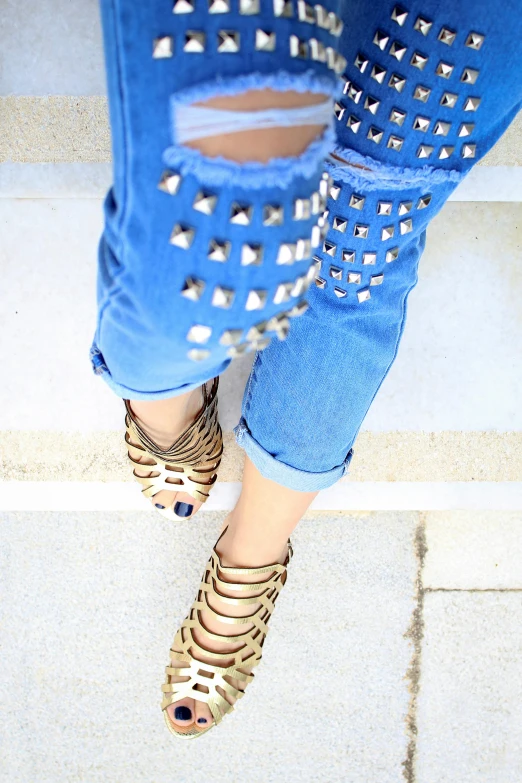 a woman standing on the steps of a building, tight blue jeans and cool shoes, wearing studded leather, gold and blue, flat lay