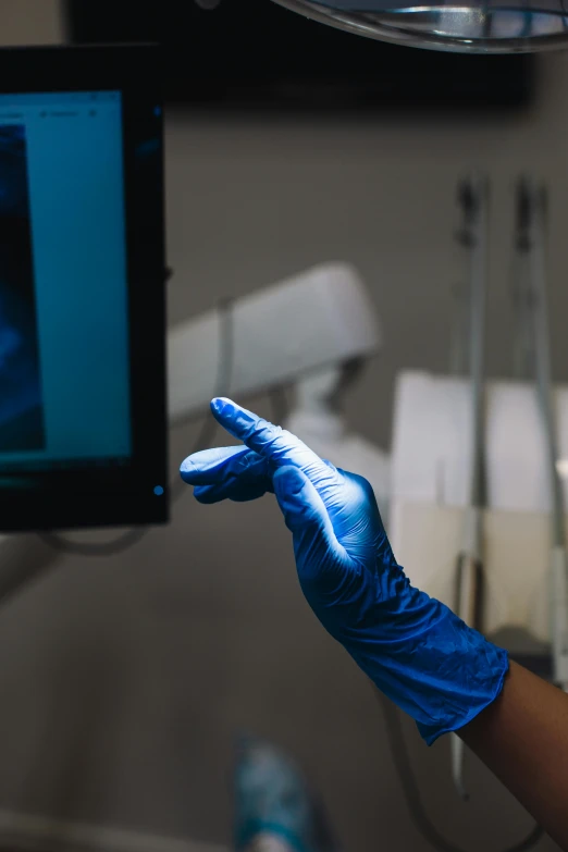 a woman in blue gloves is looking at a monitor, by Ryan Pancoast, shutterstock, holography, iv pole, photograph credit: ap, dentist, holding it out to the camera