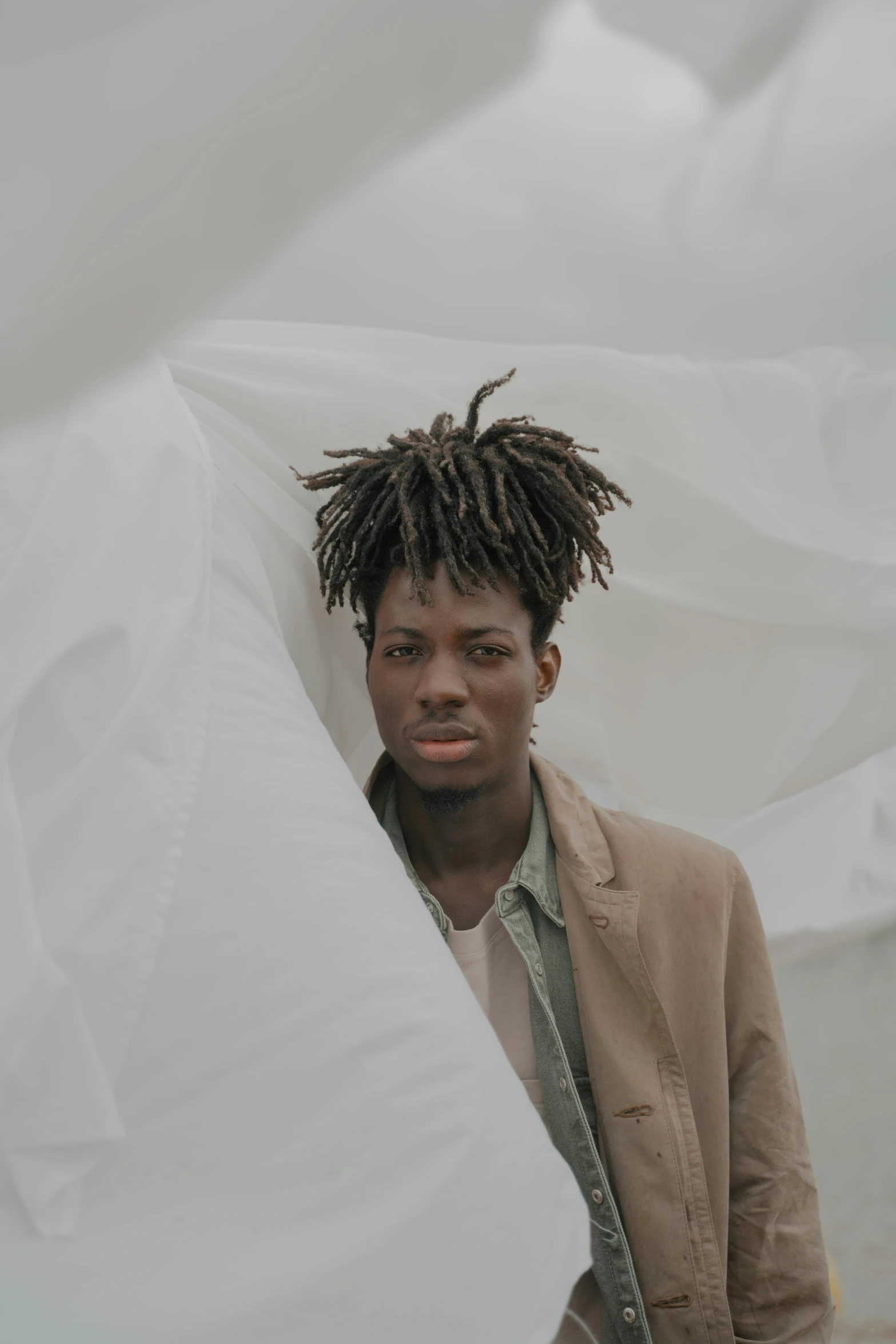 a man with dreadlocks standing in front of a white sheet, an album cover, inspired by Charles Martin, pexels contest winner, taupe, androgynous person, ( ( dark skin ) ), neutral sky