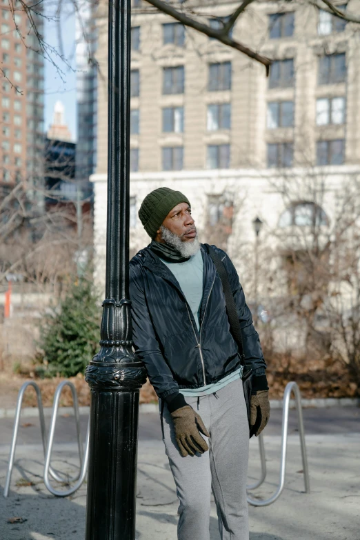 a man standing next to a lamp post on a city street, he also wears a grey beanie, samuel l jackson, lgbtq, gray beard