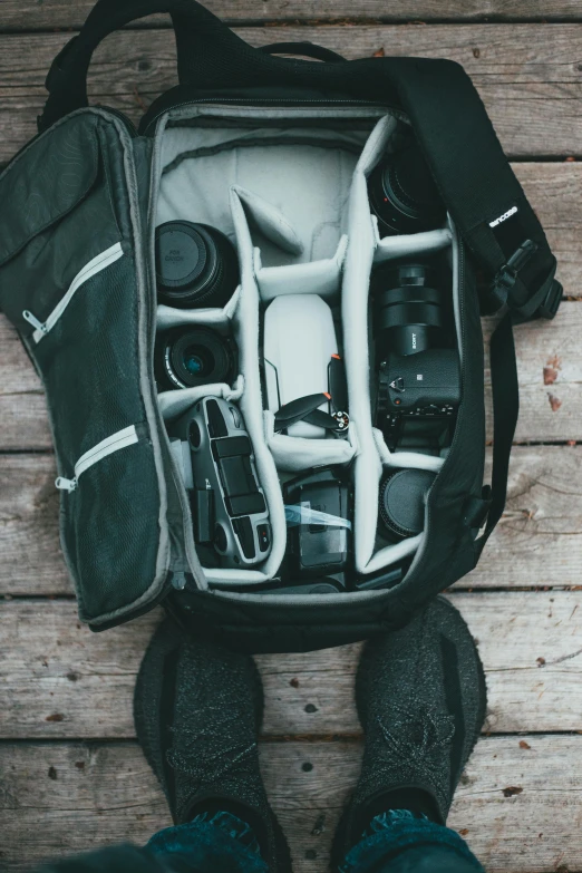 a person standing on a wooden floor with a camera in a bag, organized, backpack, center of image, photography]