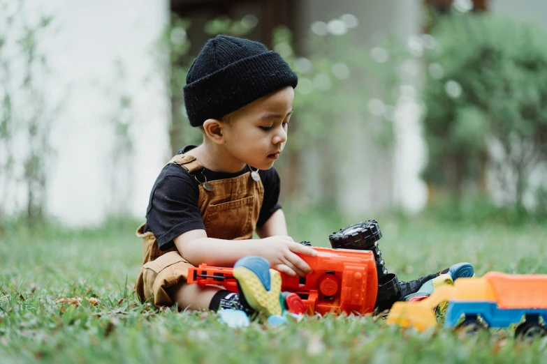 a little boy sitting in the grass playing with a toy truck, pexels contest winner, with black beanie on head, playmates toys, thumbnail, hiro