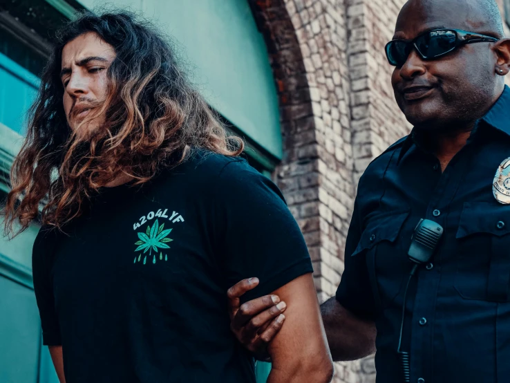 two police officers standing next to each other, pexels contest winner, renaissance, wearing a marijuana t - shirt, a black man with long curly hair, jovana rikalo, handcuffed