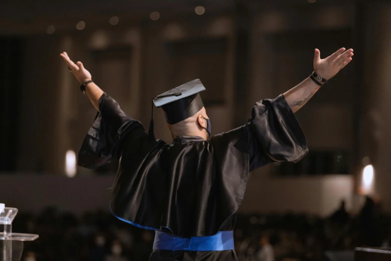 a man in a graduation gown raising his arms, unsplash, academic art, blue and black scheme, paul barson, high details, jemal shabazz