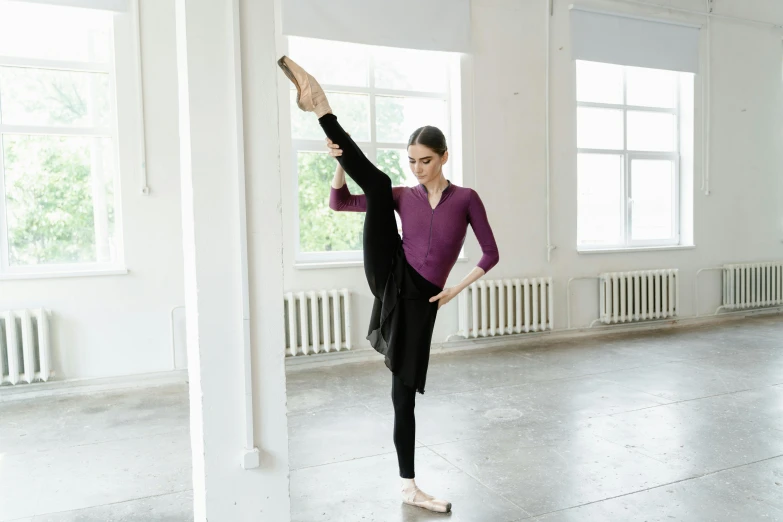 a woman standing on one leg in a dance studio, inspired by Elizabeth Polunin, pexels contest winner, arabesque, purple and black clothes, white background, anna nikonova aka newmilky, at home