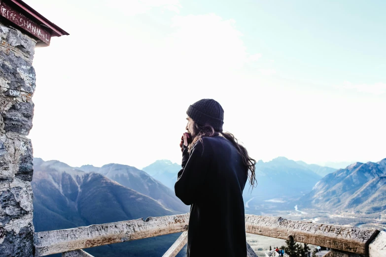 a woman standing on top of a mountain talking on a cell phone, by Julia Pishtar, pexels contest winner, woman with braided brown hair, black haired girl wearing hoodie, whistler, looking like a bird