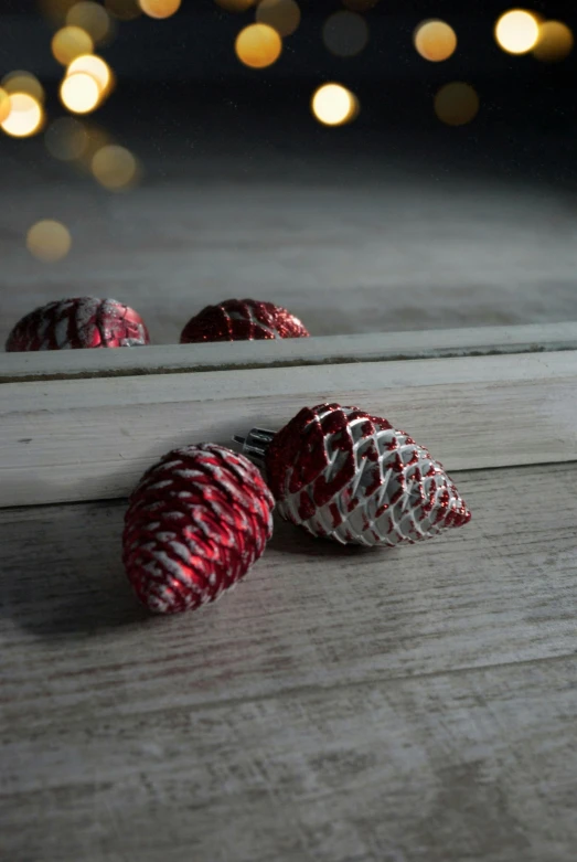 a group of pine cones sitting on top of a wooden table, silver red white details, 35 mm product photo”, mirrored, made of glazed