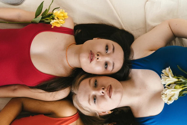a couple of women laying on top of a bed, trending on pexels, renaissance, red and blue garments, portrait sophie mudd, flowers around, asian descent