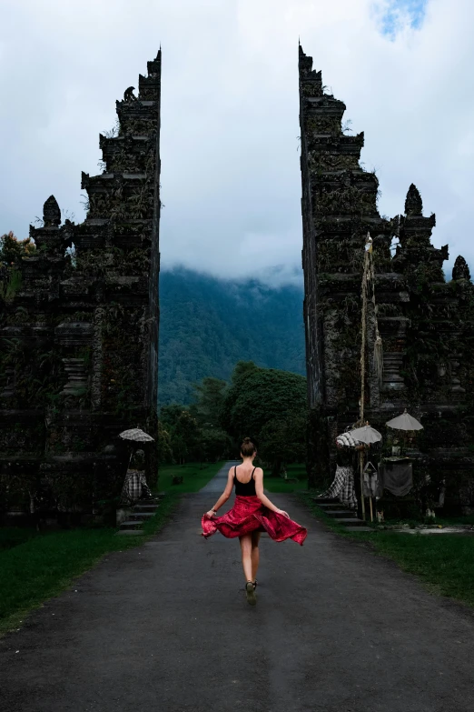 a woman in a red dress walking down a road, inspired by Steve McCurry, happening, bali, tall stone spires, in doors, dancer