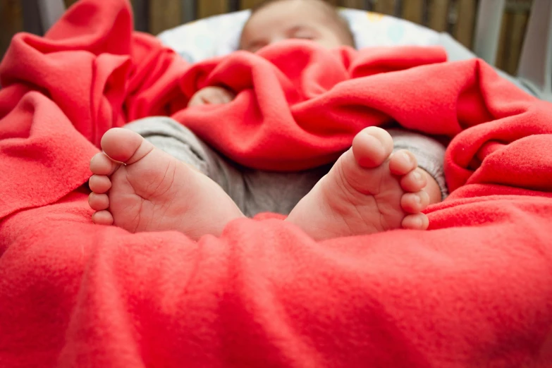 a baby laying in a crib under a red blanket, unsplash, happening, bare feet, al fresco, full colour, freezing