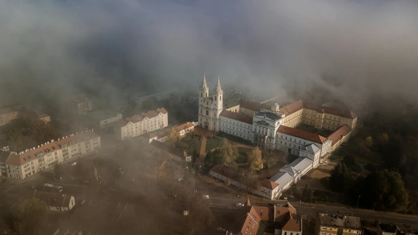 an aerial view of a city on a foggy day, by Adam Marczyński, unsplash contest winner, baroque, old abbey in the background, military buildings, volumetric light and fog, university