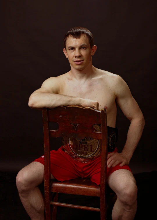 a man sitting on top of a wooden chair, an album cover, inspired by Svetlin Velinov, mma, leaked photo, nathan for you, world championship fight