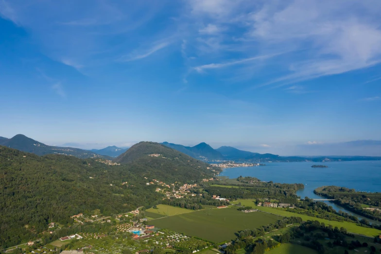 a large body of water next to a lush green hillside, by Carlo Martini, pexels contest winner, renaissance, “ aerial view of a mountain, abbondio stazio, island in the background, giorgetto giugiaro