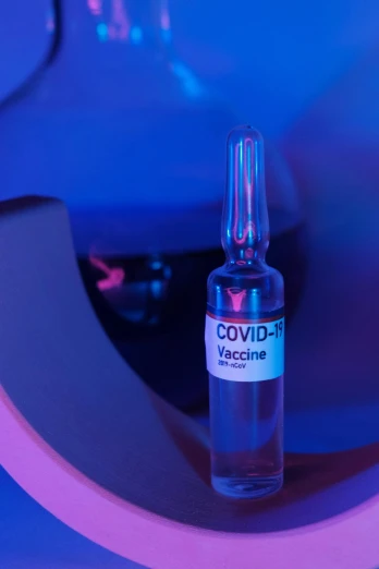 a bottle of liquid sitting on top of a table, syringe, purple and blue neon, inside a science facility, covid