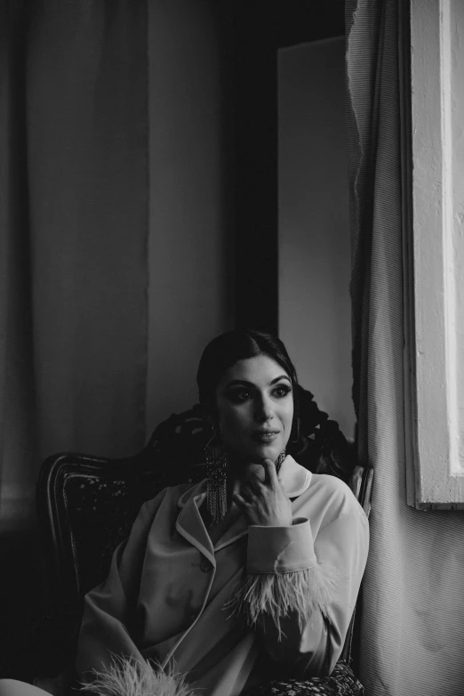 a woman sitting in a chair next to a window, a black and white photo, inspired by Elsa Bleda, unsplash, renaissance, dua lipa, looking to camera, greek ameera al taweel, sittin