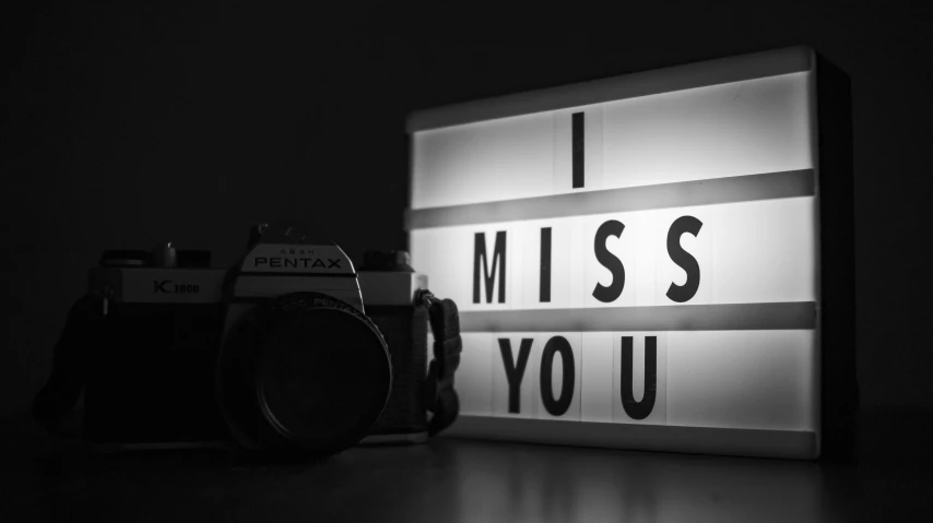 a camera sitting on top of a table next to a light box, a black and white photo, by Julia Pishtar, pixabay, graffiti, i love you, missing panels, i see you, very sad