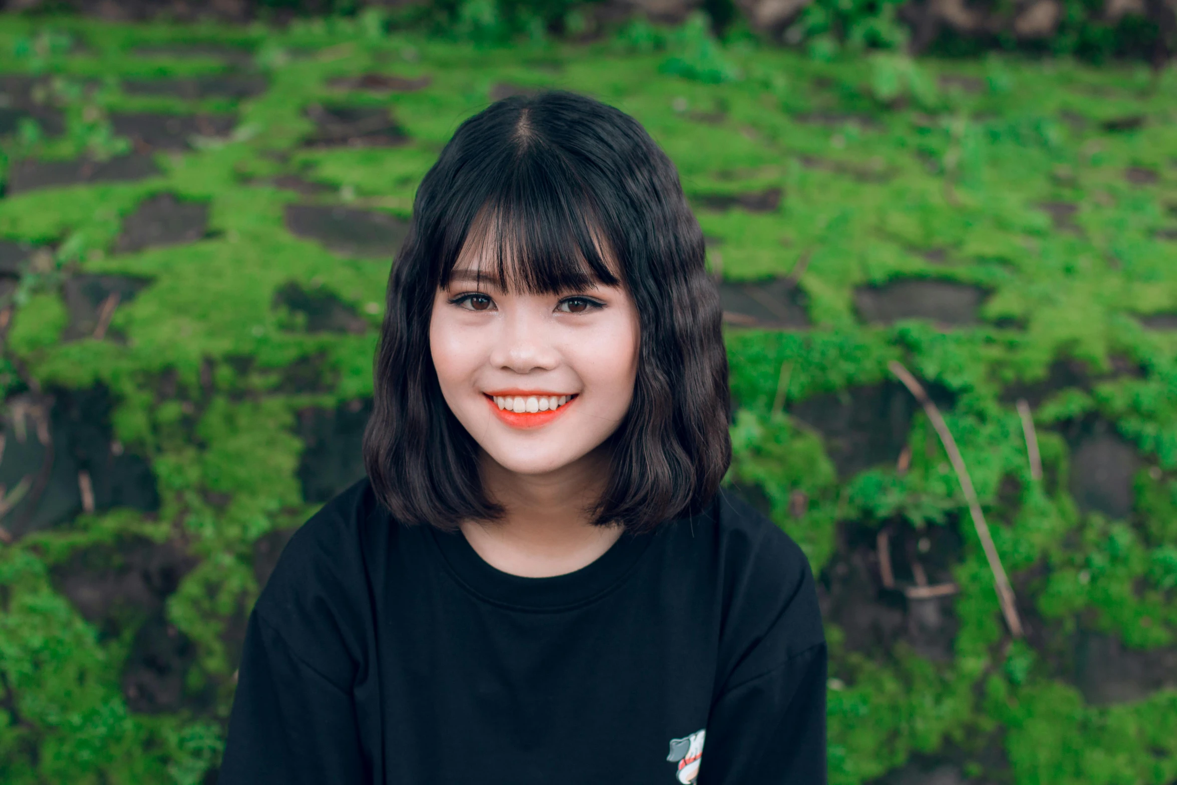 a woman standing in front of a lush green field, a picture, inspired by Ruth Jên, pexels contest winner, realism, black bangs, coral brown hair, young cute wan asian face, 1 6 years old