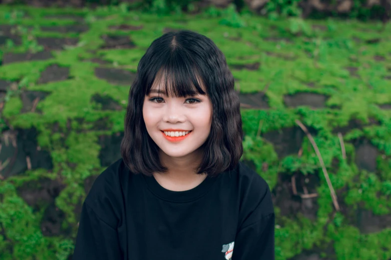 a woman standing in front of a lush green field, a picture, inspired by Ruth Jên, pexels contest winner, realism, black bangs, coral brown hair, young cute wan asian face, 1 6 years old