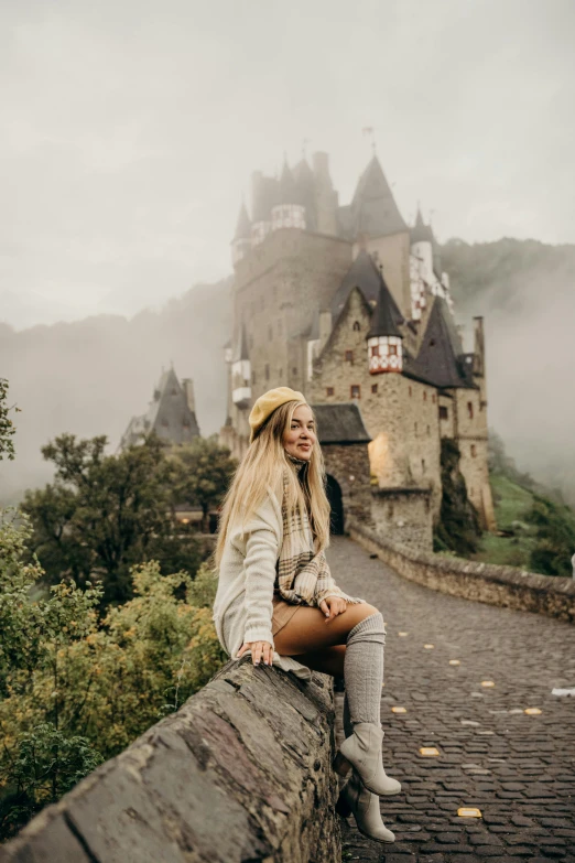 a woman sitting on a wall in front of a castle, pexels contest winner, 🍁 cute, goldilocks, grey mist, lower saxony