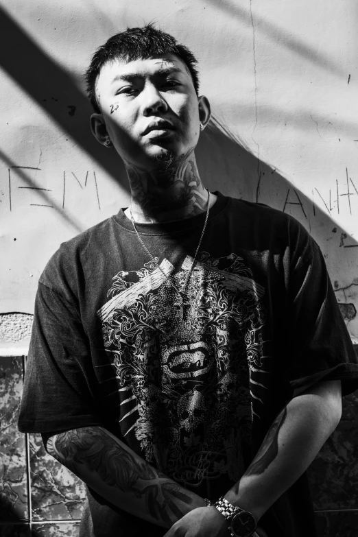 a man standing in front of a wall with graffiti on it, a black and white photo, inspired by Xi Gang, fully tattooed body, sun behind him, vocalist, ((portrait))