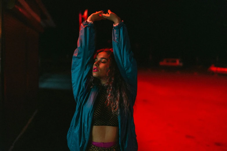 a woman standing in front of a red light, an album cover, inspired by Elsa Bleda, pexels contest winner, graffiti, wearing a neon blue hoodie, playful pose of a dancer, night time low light, lorde