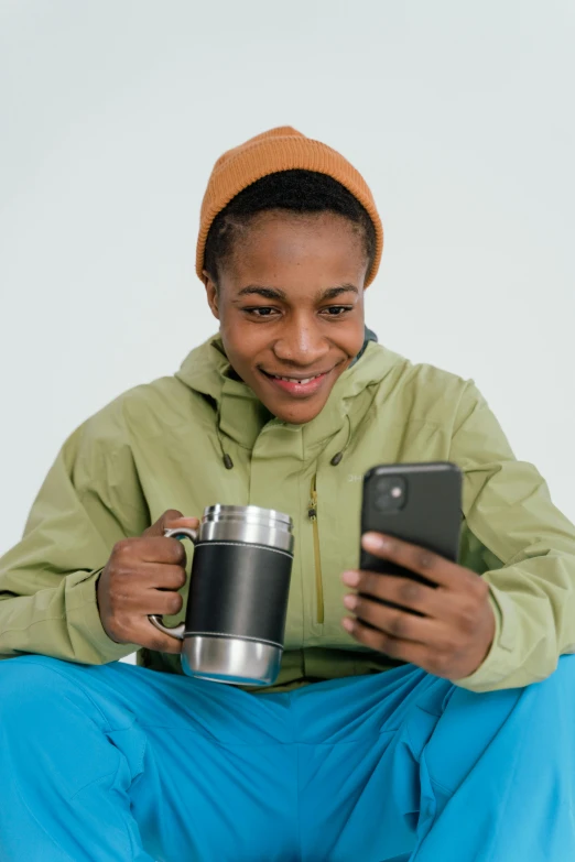 a woman sitting on the ground holding a cup and a cell phone, wearing adventuring gear, black teenage boy, warm features, official product image