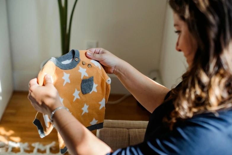 a woman sitting on a couch holding a stuffed animal, a cartoon, by Julia Pishtar, pexels contest winner, happening, touching her clothes, grey orange, with stars, maternity feeling