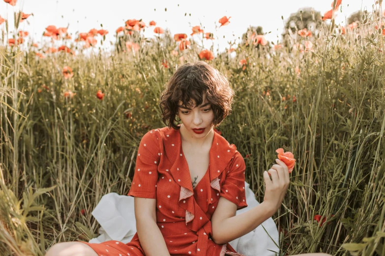 a woman sitting in a field of red flowers, by Julia Pishtar, orange jumpsuit, sophia lillis, high quality product image”, portrait image