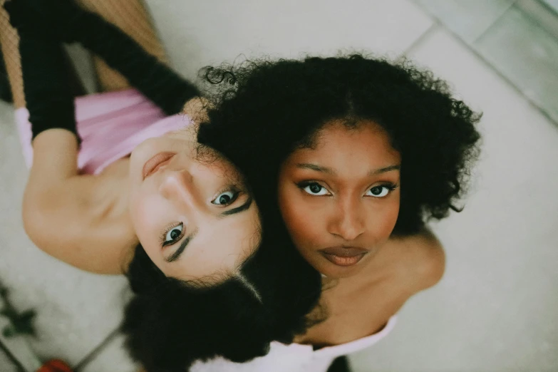 a couple of women standing next to each other, by Lily Delissa Joseph, trending on pexels, renaissance, black curly hair, laying on her back, eyes looking at the camera, skin color