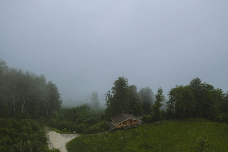 a house sitting on top of a lush green hillside, inspired by Gregory Crewdson, hurufiyya, moist foggy, log cabin beneath the alps, overview, grey