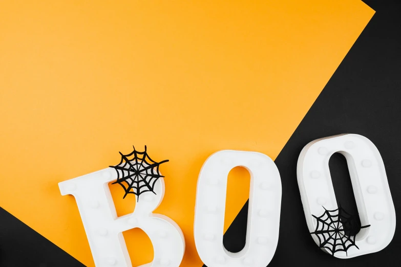 the word boo spelled in white letters on a yellow and black background, by Julia Pishtar, trending on pexels, beistle halloween decor, white and orange, modelling, spiderwebs