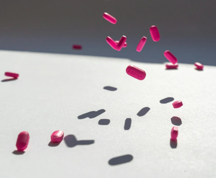 a white table topped with lots of pink pills, a microscopic photo, by Rachel Reckitt, pexels, drops are falling from above, directional sunlight skewed shot, crimson themed, asset on grey background