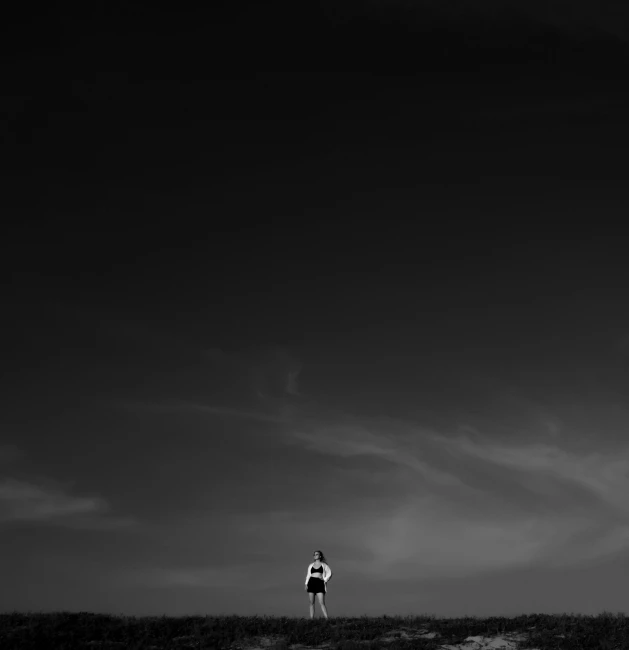 a man standing on top of a hill under a cloudy sky, a black and white photo, unsplash contest winner, minimalism, high contrast 8k, astronaut walking, a lonely woman, running