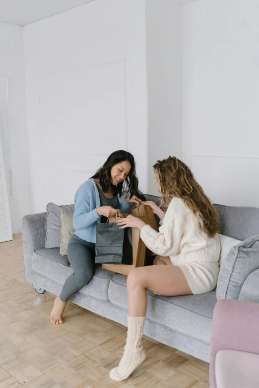 two women sitting on a couch in a living room, by Matija Jama, pexels contest winner, happening, shopping groceries, promo image, head to waist, giving gifts to people